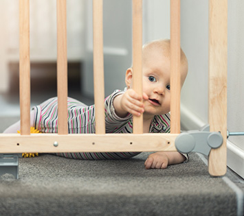 A Baby Held Back By a Childproof staircase Gate, Which Is Part Of Keeping Your Home Safe