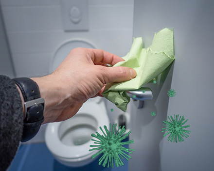 An Image of Hand with Wipe Wiping Surfaces to Sanitize Bathroom Stall Handle